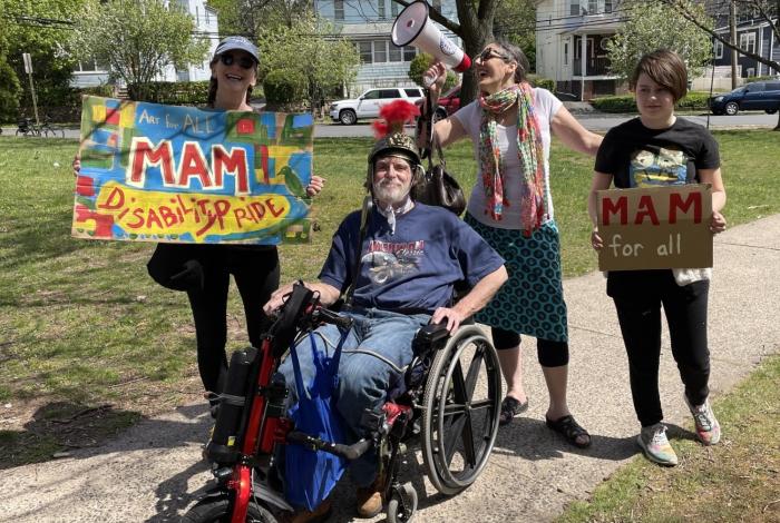 MAM staff members at the Montclair Disability Pride Parade in 2022 (A man in a wheel chair is in the middle of the photo, with three women standing behind him holding signs saying "MAM for all" and "Art for all. MAM Disability Pride")